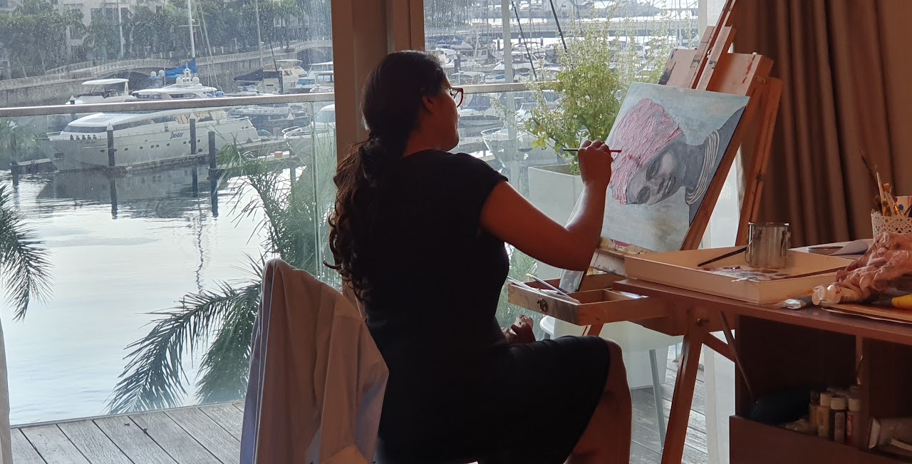 Anjali painting a portrait positioned sideways on her easel beside a window